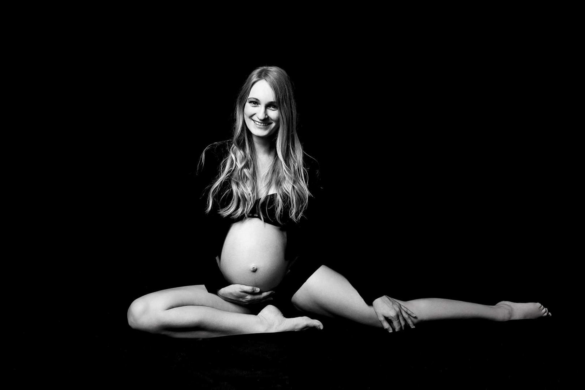 Těhotenský akt Brno, nastávající maminka sedí v ateliéru na černém pozadí a usmívá se, černobílé umělecké focení, Marcela Kramářová